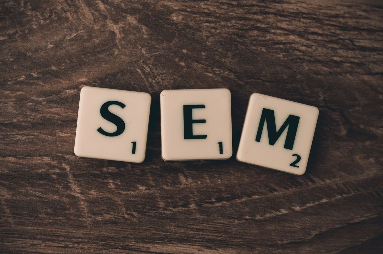 Fond en bois avec des lettres en cubes formant SEM, illustrant le marketing sur les moteurs de recherche.
