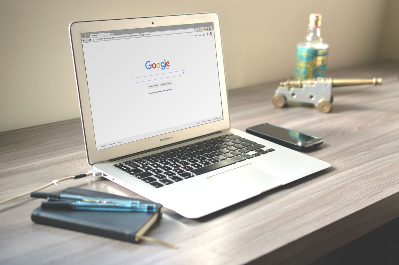 A tidy workspace with a laptop showing Google search, a smartphone, and a notebook arranged on a wooden desk.
